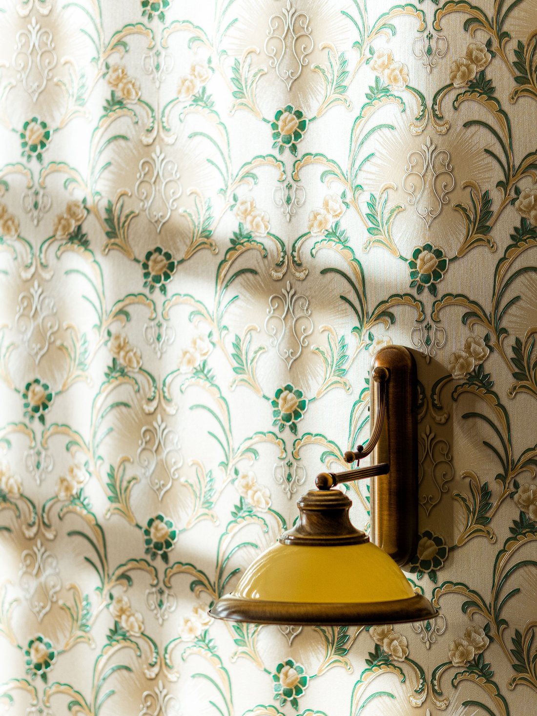 Green floral wallpaper with a brass wall sconce